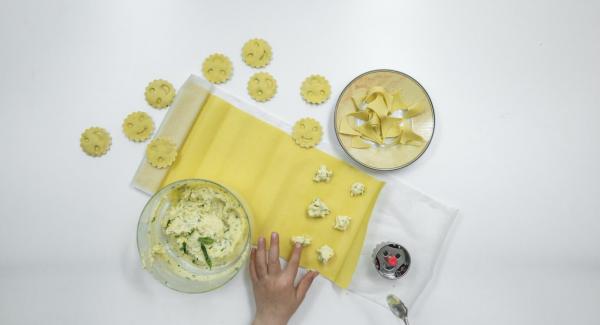 Extender la masa para pasta y, si es necesario, marcar la forma de los raviolis de unos 5 cm Ø en la mitad de la masa. Colocar pequeños trozos de relleno encima y mojar la pasta con un poco de agua con la ayuda de un cepillo.