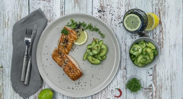 Trocear las hojas de eneldo. Sazonar los filetes de salmón con sal y pimienta, servir con la ensalada de pepino y guindilla, y esparcir el eneldo y el sésamo por encima.