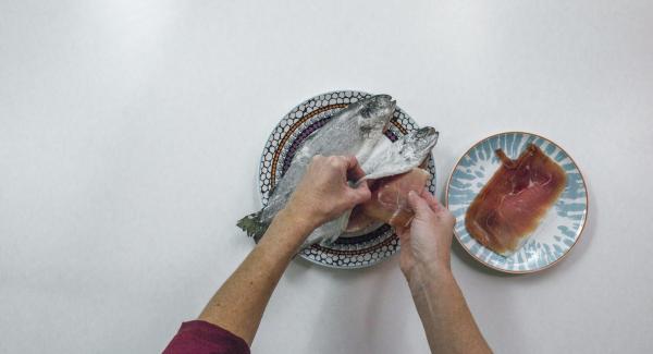 Rellenar la trucha con 2 lonchas de jamón y rebozar en harina. Pelar y cortar los dientes de ajo en rodajas.